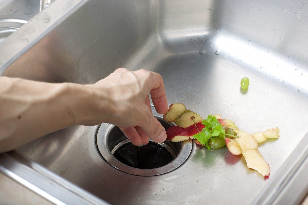 hand removing trash from kitchen sink