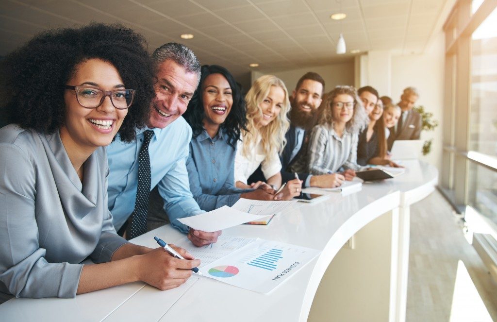 line of smiling employees standing at the side of white table