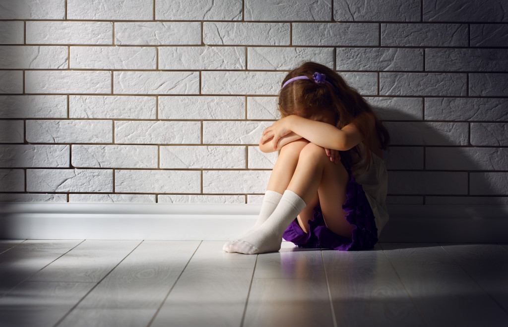 daughter covering her face with her arms while seated in a cold floor